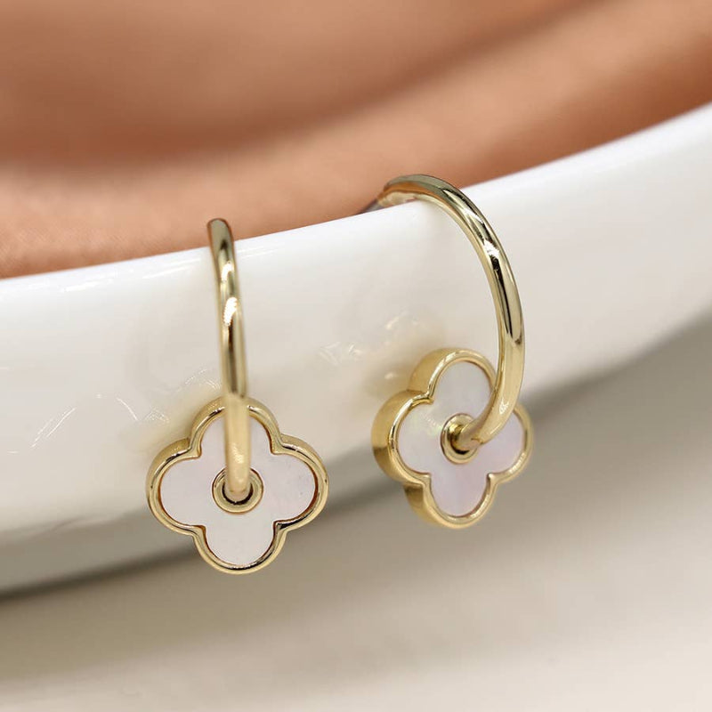 Gold hoop earrings with white clover-shaped charms on a neutral background