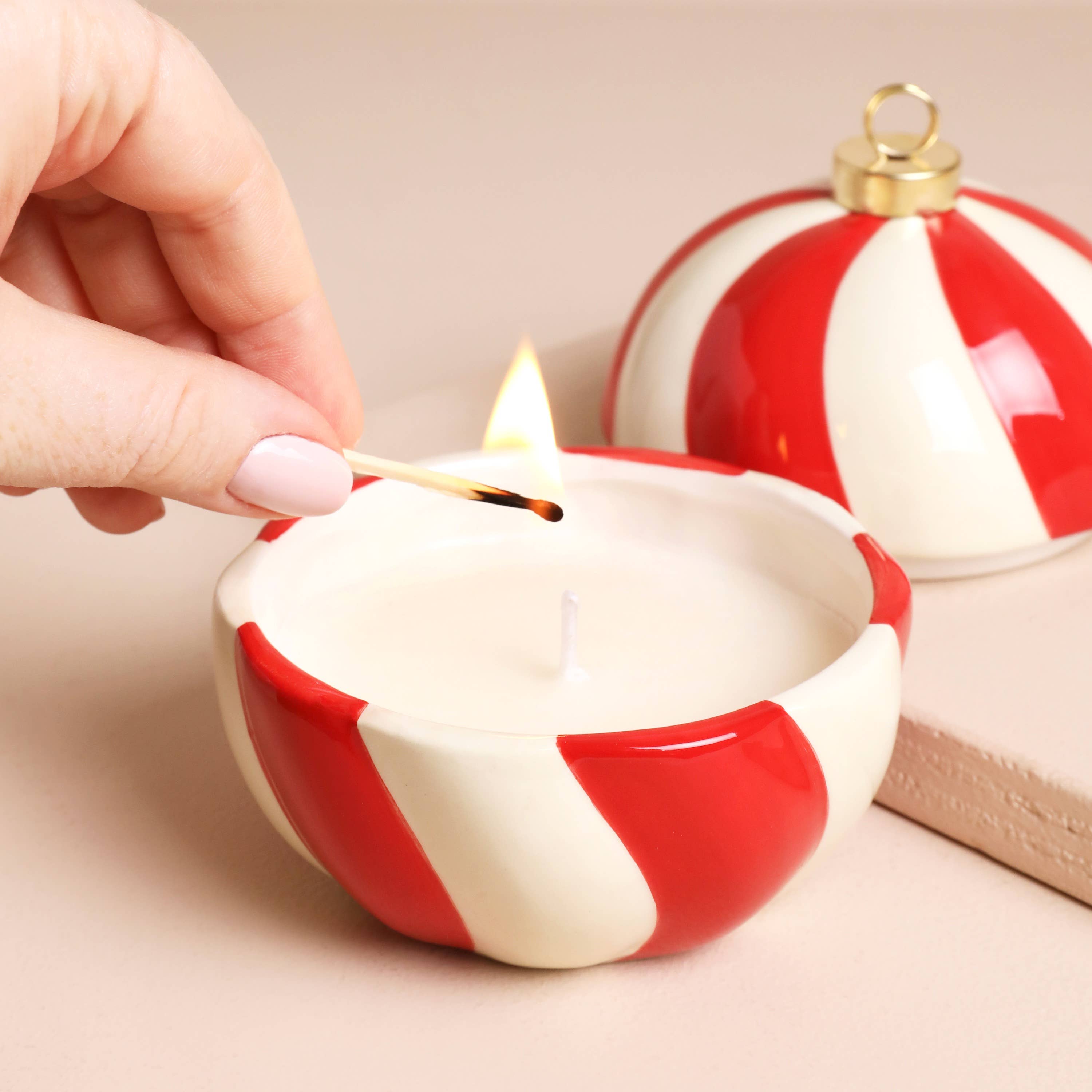 Red and white striped candle being lit with a match, with a matching ornament in the background.