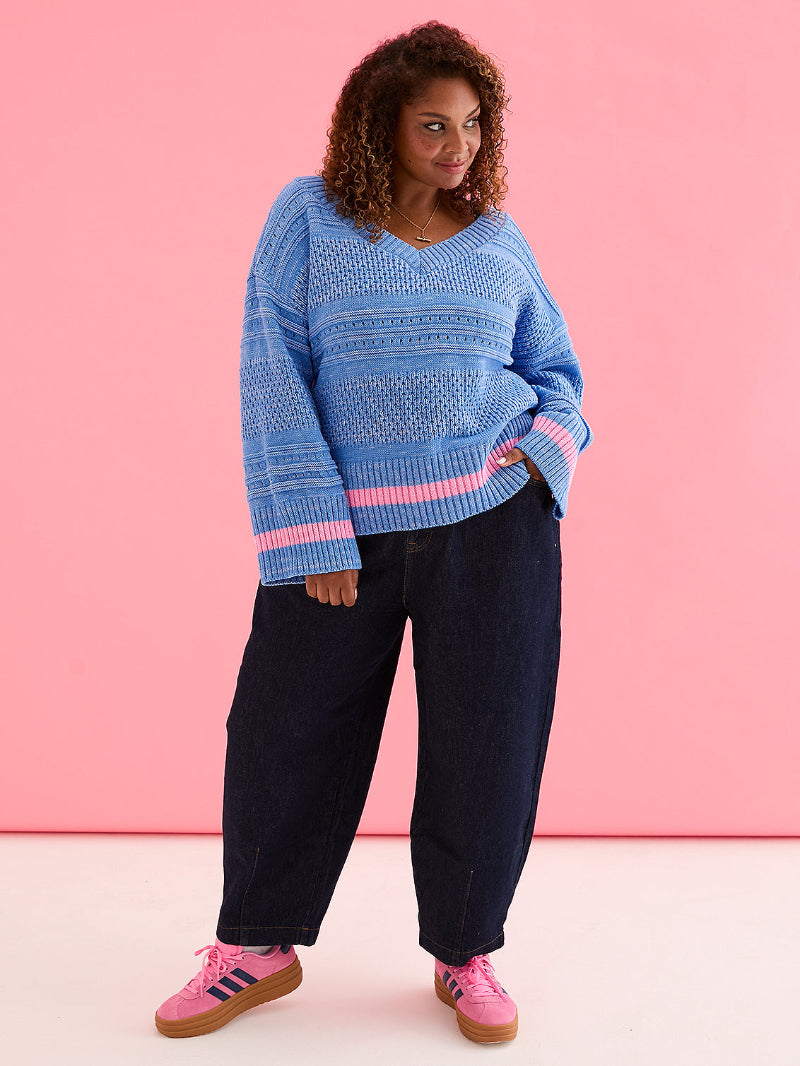 Person wearing Cara & The sky JudithJumper Blue_Front  a blue patterned sweater with pink accents against a pink background