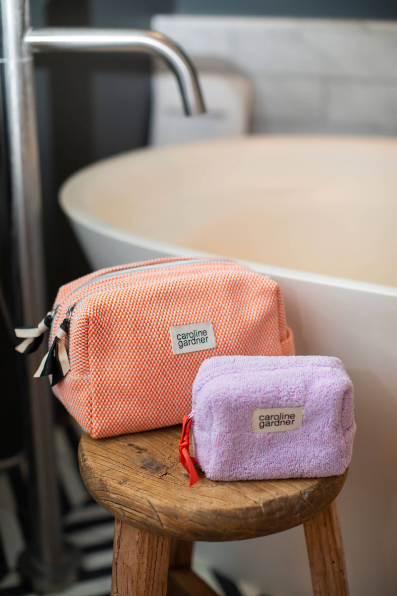 Two small pouches, one pink and one purple, on a wooden stool with a bathroom background.