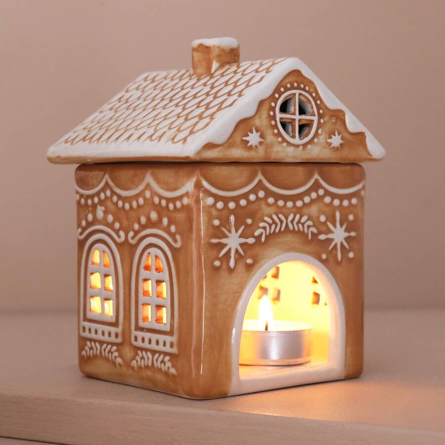 Decorative gingerbread house-shaped lantern with a lit candle inside on a beige background