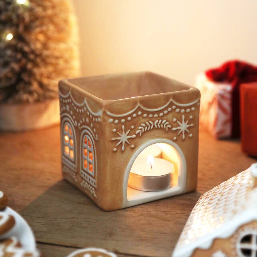Decorative gingerbread house candle warmer with a lit candle inside on a wooden surface.