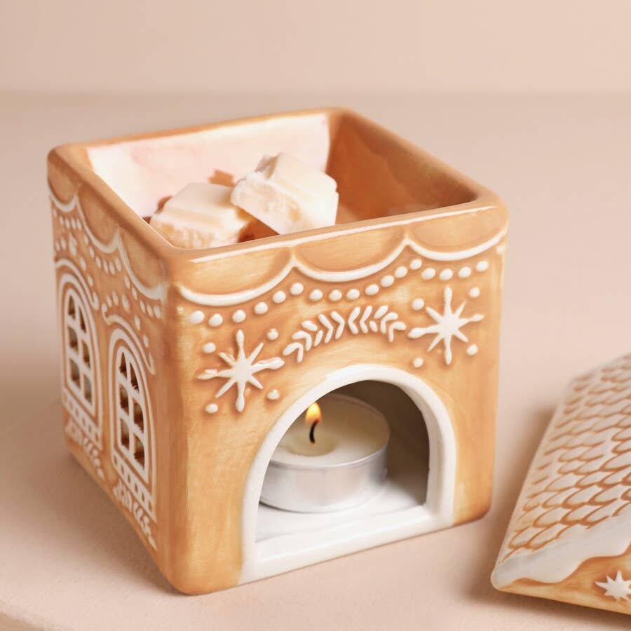 Decorative ceramic wax warmer with a lit candle on a beige background