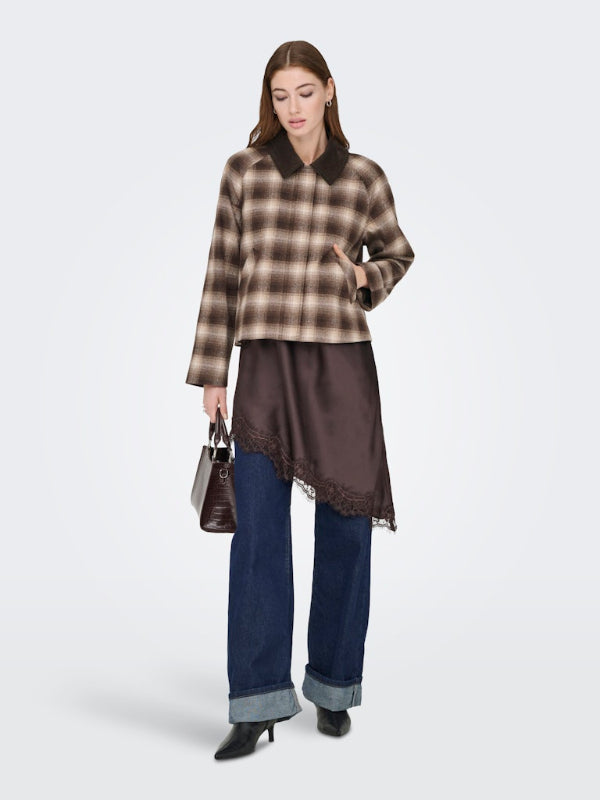 Woman wearing a plaid shirt, satin top, and jeans on a white background