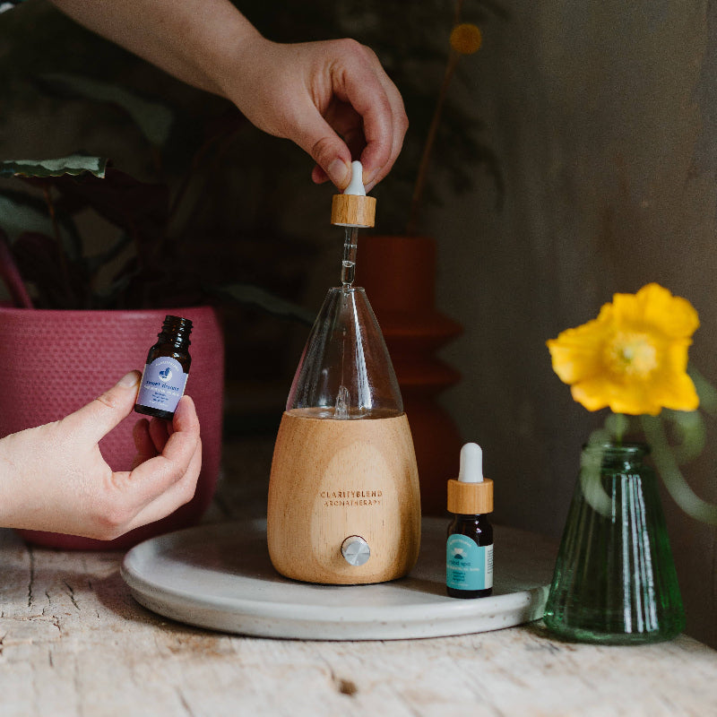 Person using a wooden diffuser with essential oil bottles on a table.
