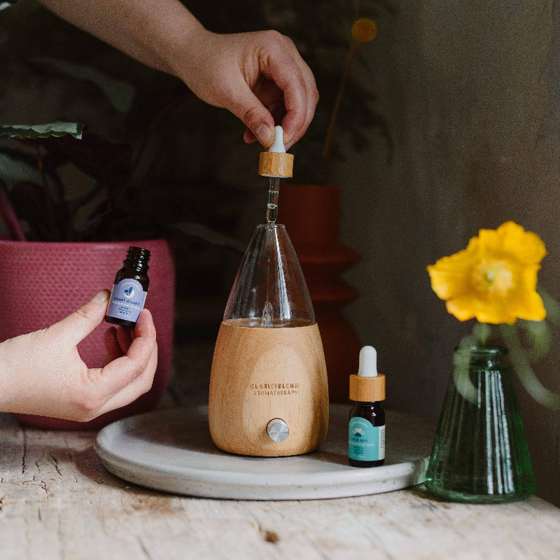 Person using a wooden diffuser with essential oil bottles on a table.