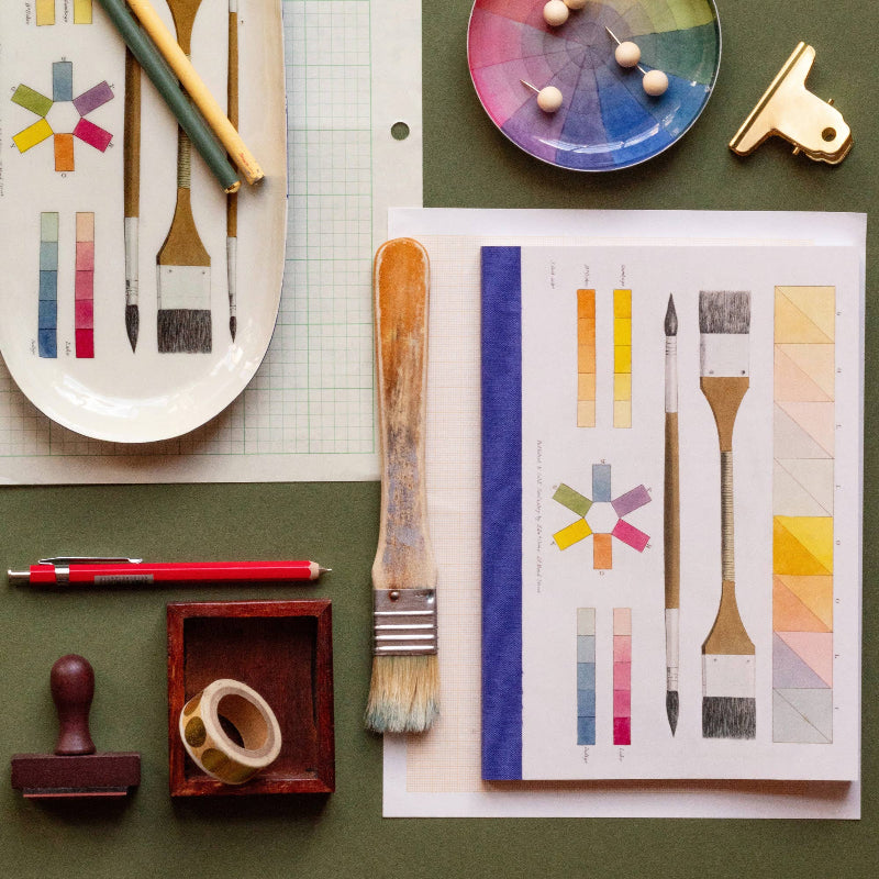 Art supplies including brushes, a color wheel, and printed design on a green surface.