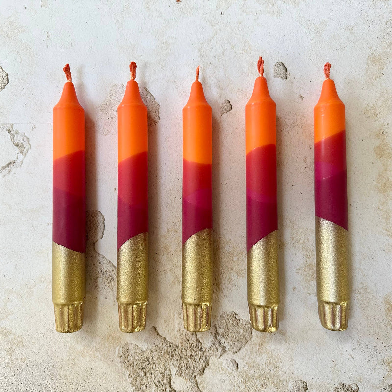 Five colorful candles with red, orange, and gold layers on a textured surface