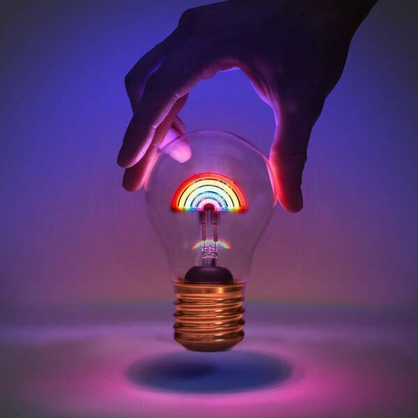 Light bulb with rainbow inside held by a hand against a purple background