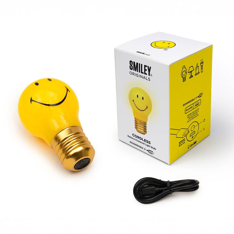 Yellow smiley face light bulb with gold base and black cord next to its packaging on a white background