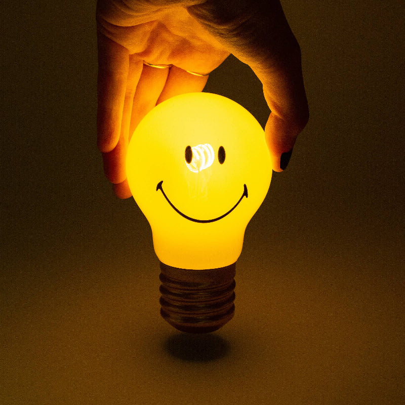 Hand holding a yellow light bulb with a smiley face on a dark background