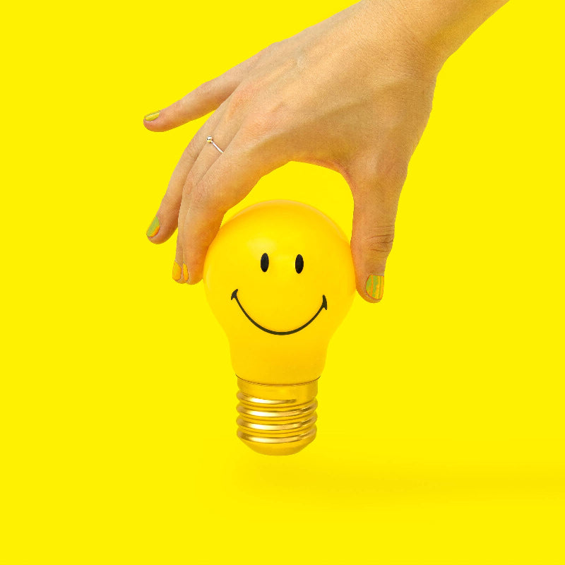 Hand holding a yellow light bulb with a smiley face on a yellow background