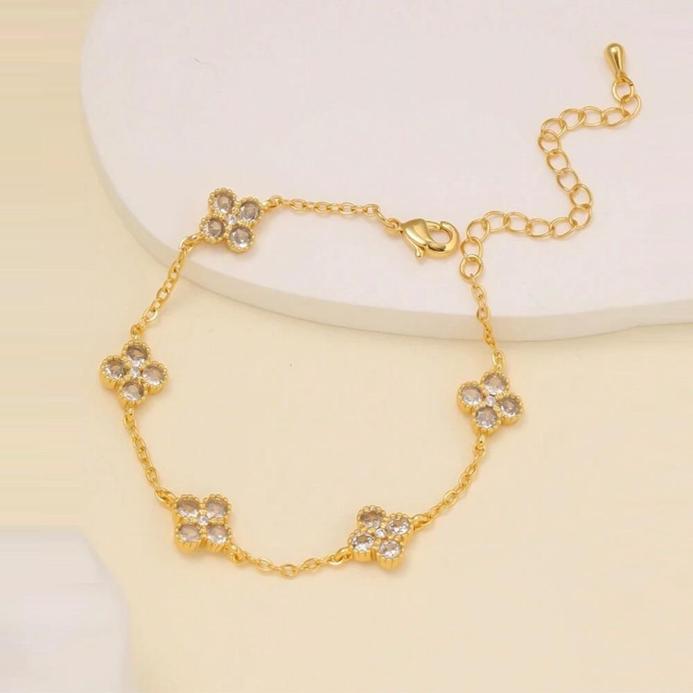 Gold bracelet with clover-shaped charms on a beige background