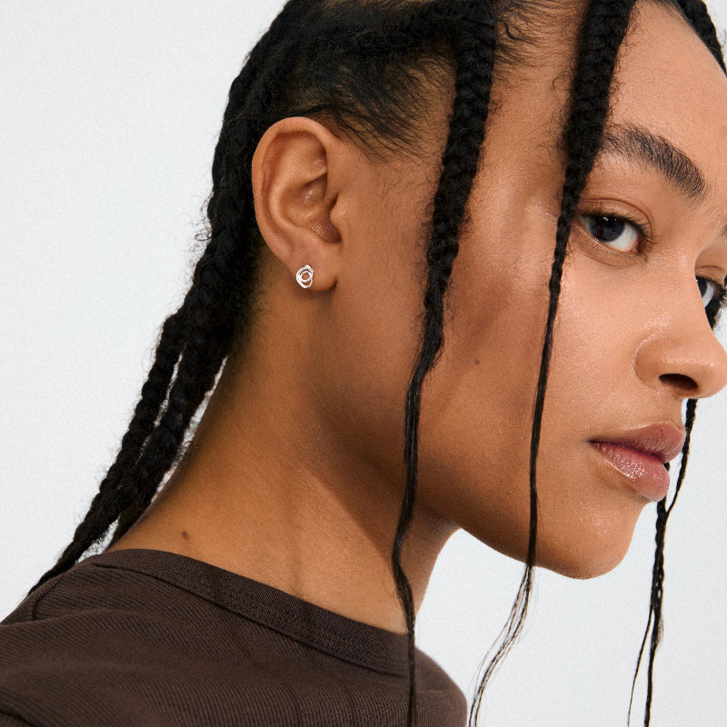 Close-up of a person with braided hair wearing earrings against a neutral background