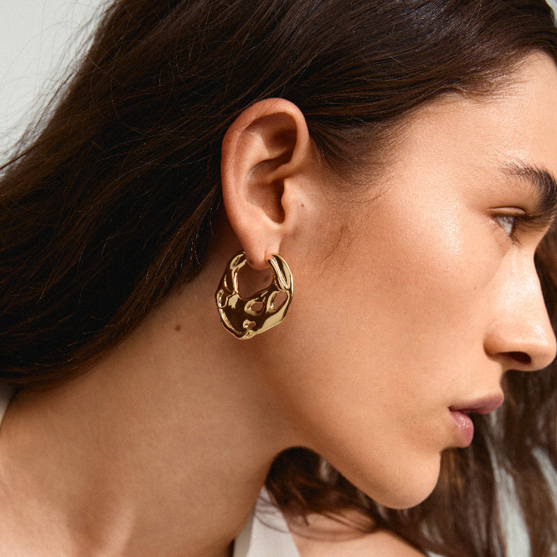Close-up of a person wearing a gold hoop earring with a neutral background