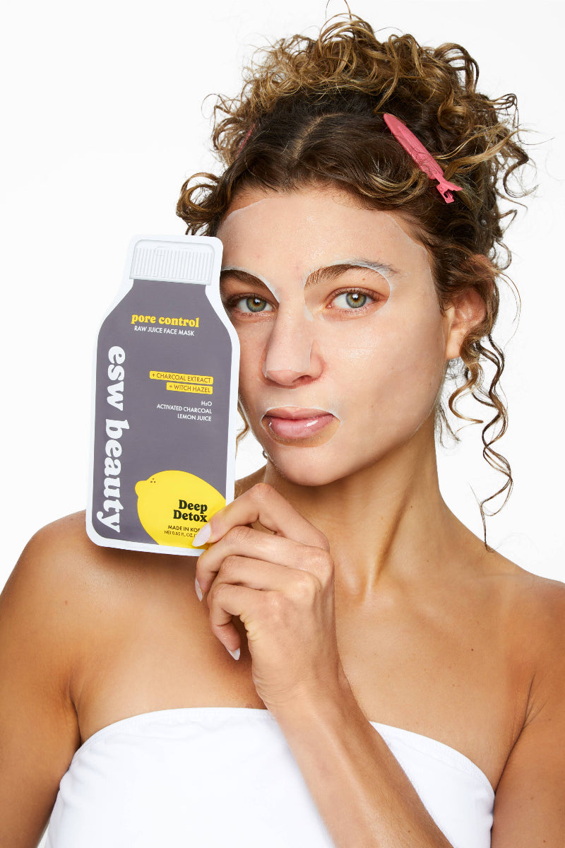 Woman holding a bottle of 'ew beauty' product with a plain background