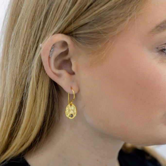 Close-up of a person wearing gold earrings with a blurred background