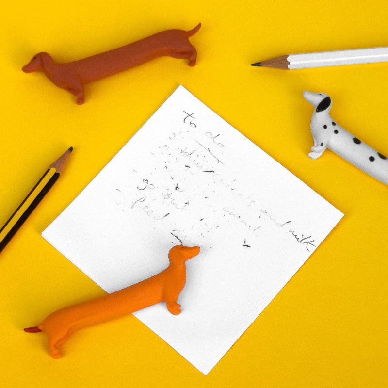 White paper with writing, orange dachshund-shaped eraser, and two pencils on a yellow background