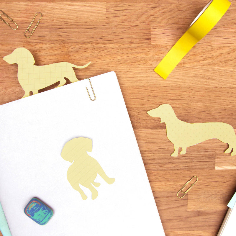 Dog-shaped cutouts on a notebook with stationery items on a wooden surface