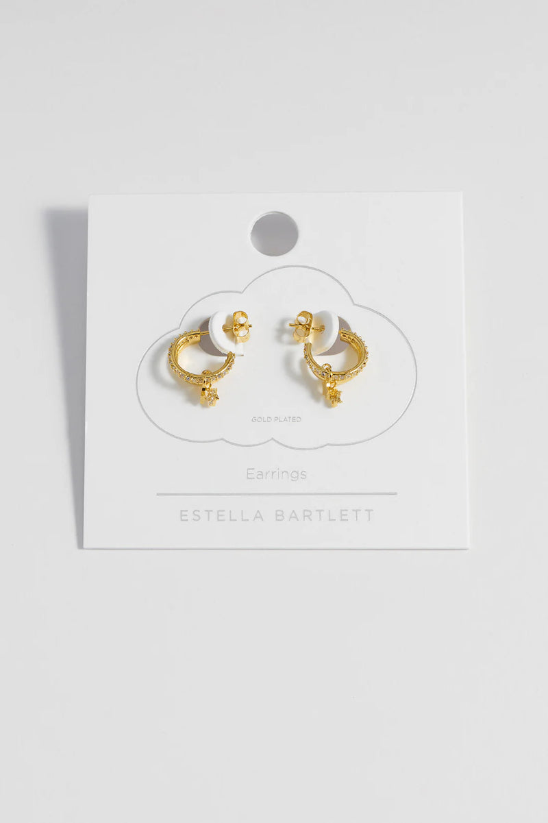 Gold earrings on a white card with 'Estella Bartlett' branding against a white background