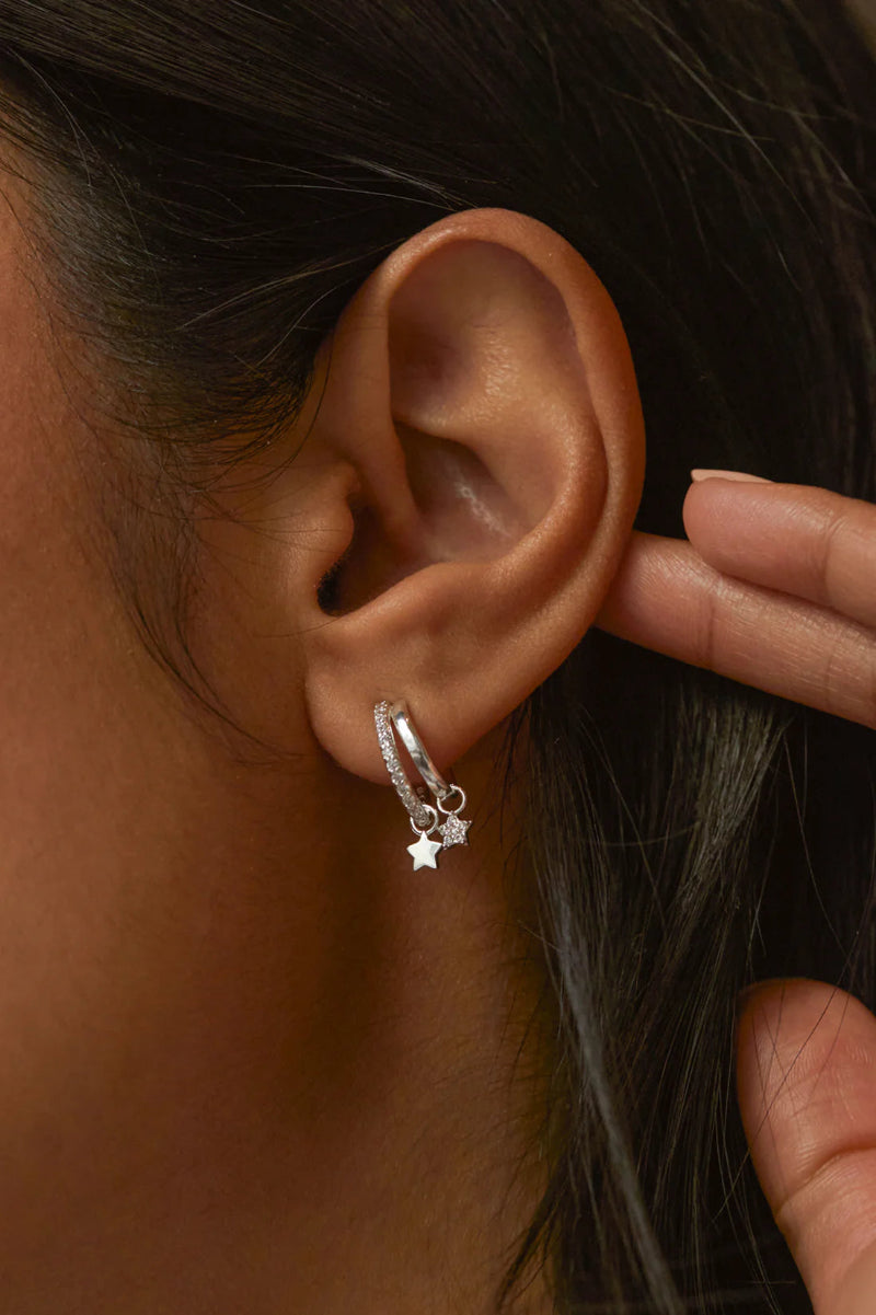 Close-up of an ear wearing a silver hoop earring with star details.