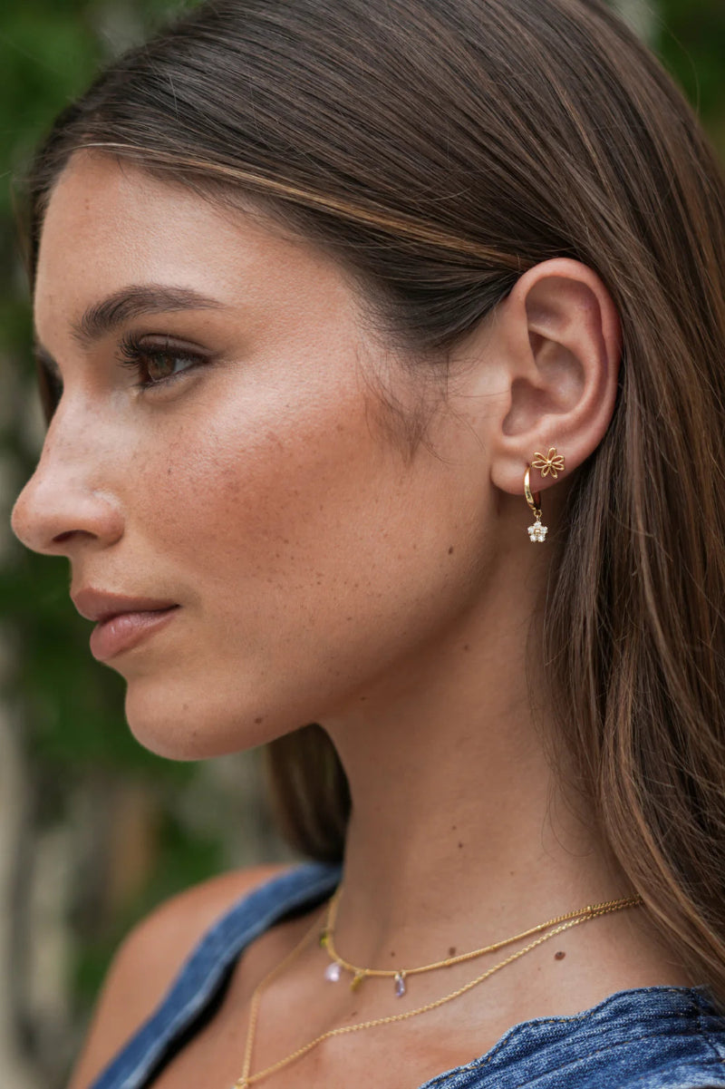 Close-up of a woman wearing gold earrings and necklaces with a blurred natural background