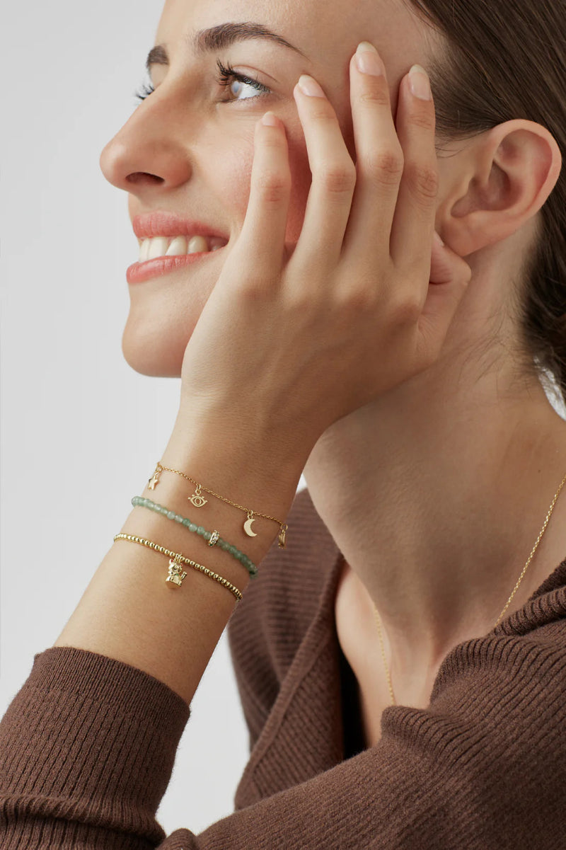 Woman wearing multiple gold bracelets on her wrist with a neutral background