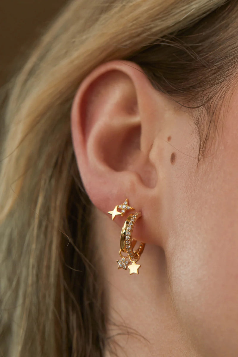 Close-up of an ear wearing gold hoop earrings with star details.
