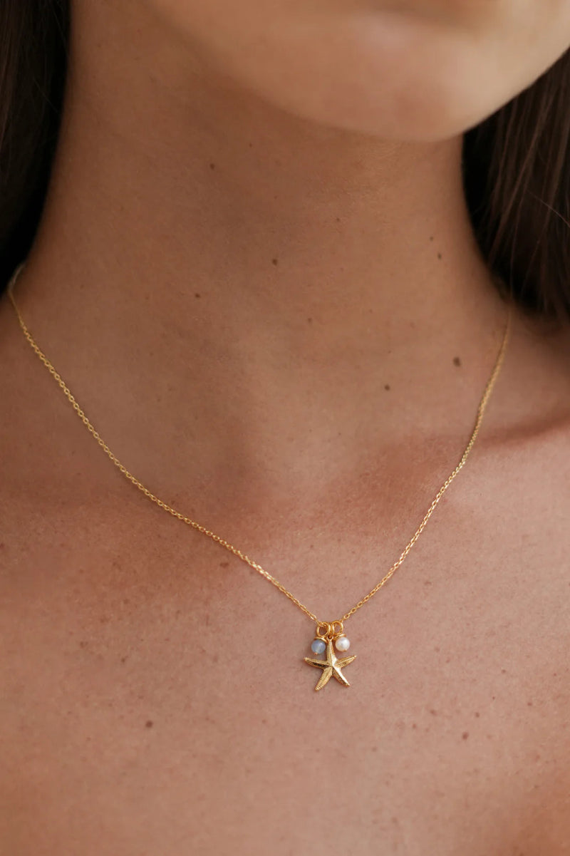 Gold necklace with a starfish pendant worn by a person