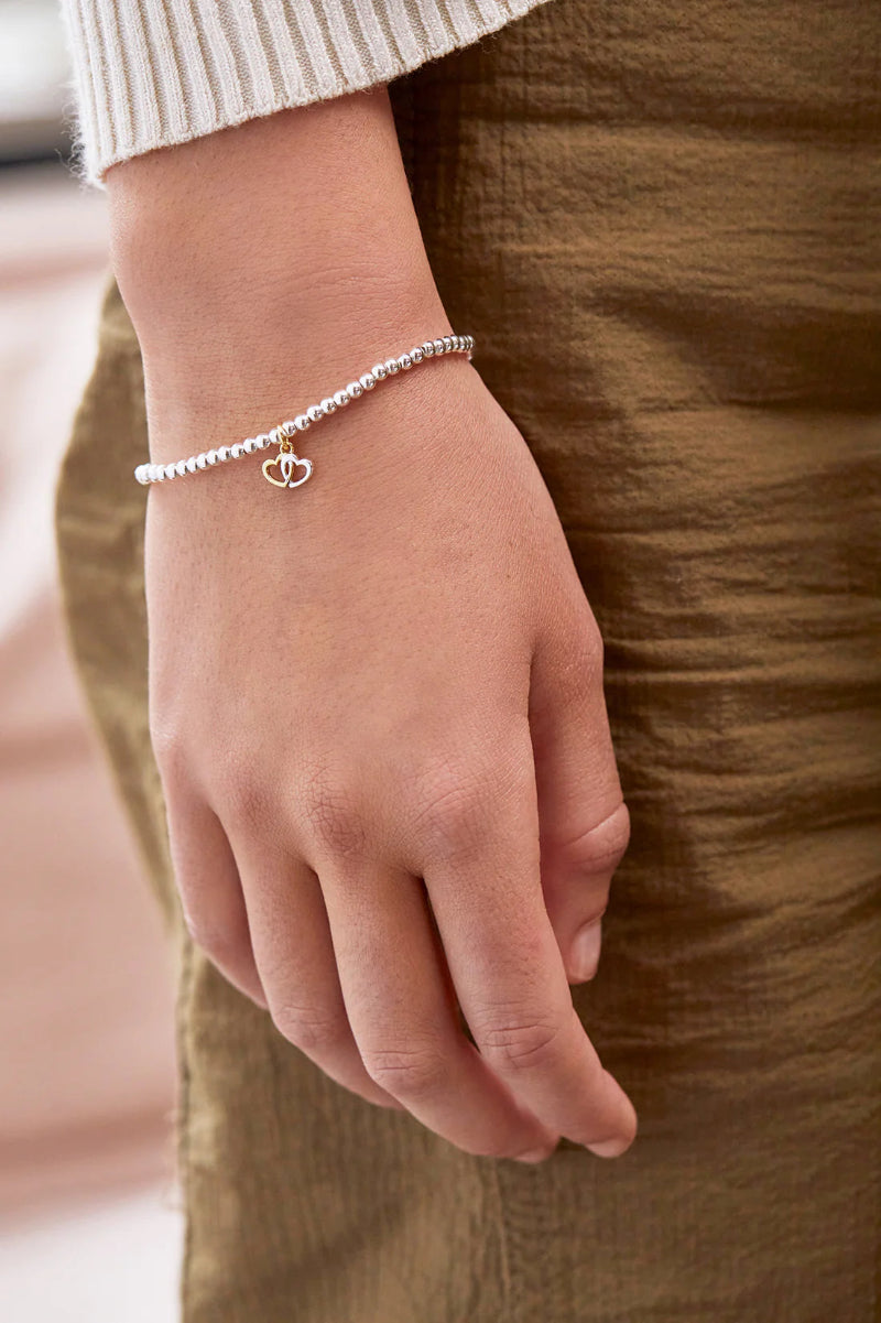 Hand wearing a silver bracelet with a heart charm on a blurred background