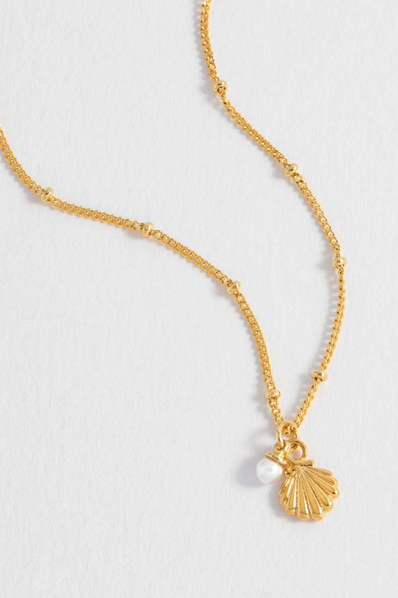 Gold necklace with a shell pendant on a light gray background