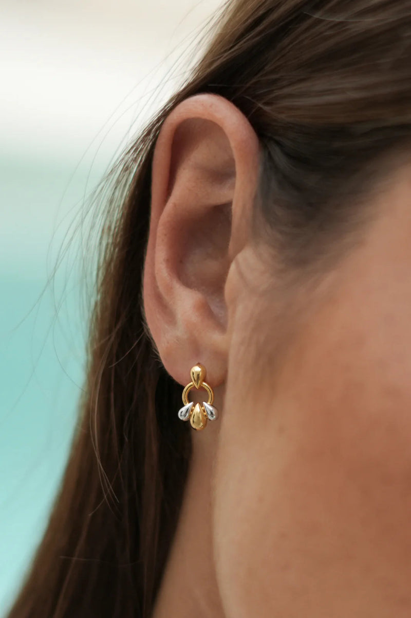 Close-up of an ear wearing a gold earring with a blurred background