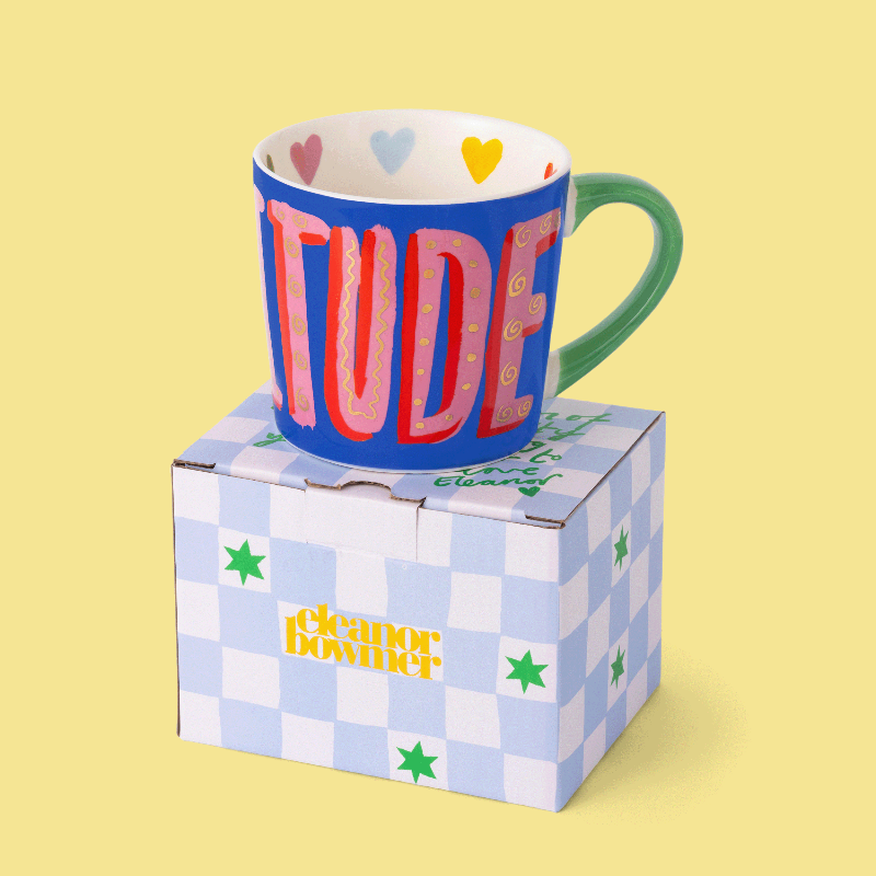 Colourful mug with 'GRATITUDE' on a checkered box against a yellow background