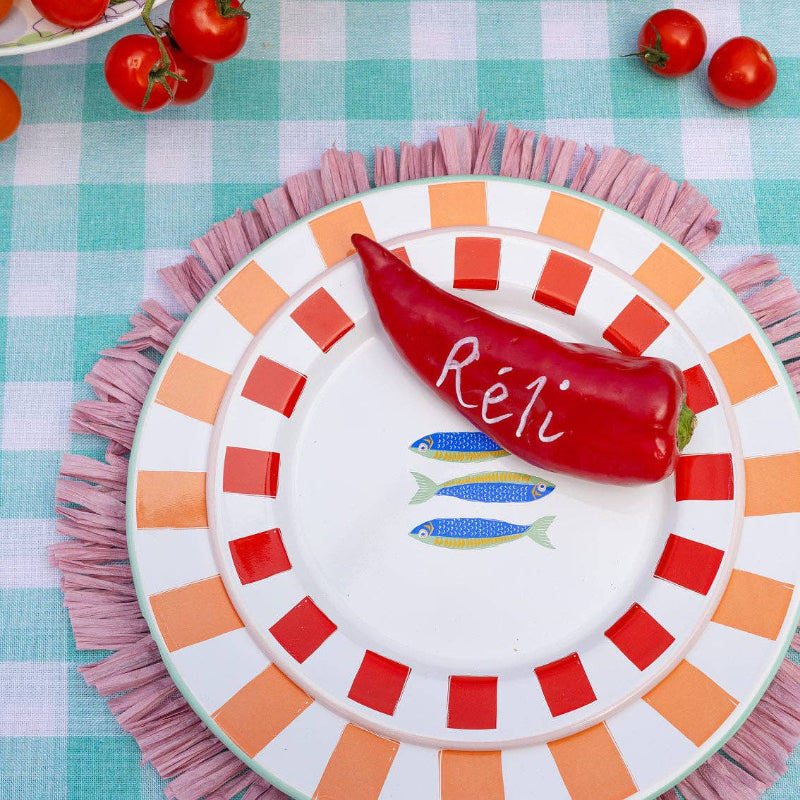 Decorative plate with a red pepper and 'Reli' branding on a checkered tablecloth.