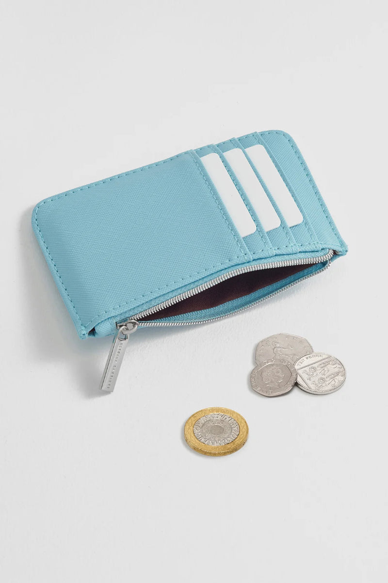 A light blue leather zip-around card holder wallet with three card slots, shown open with several coins placed beside it on a clean white background.