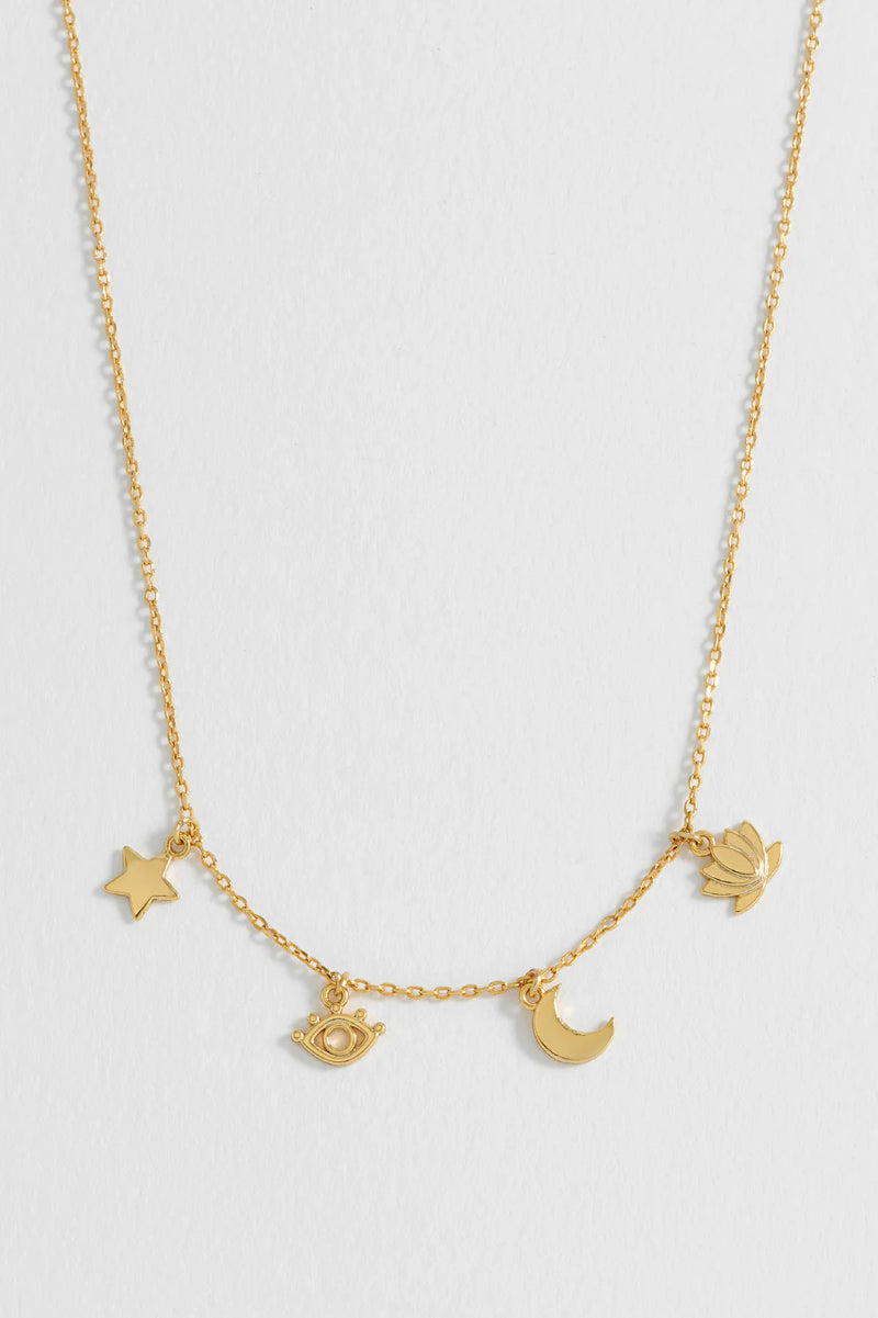 Gold necklace with star, moon, and eye charms on a light gray background