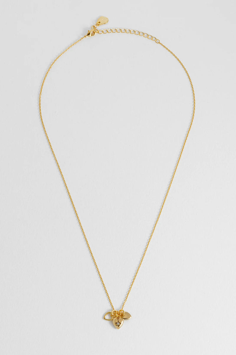 A delicate gold chain necklace featuring small gold heart pendant, displayed against a clean, light gray background.