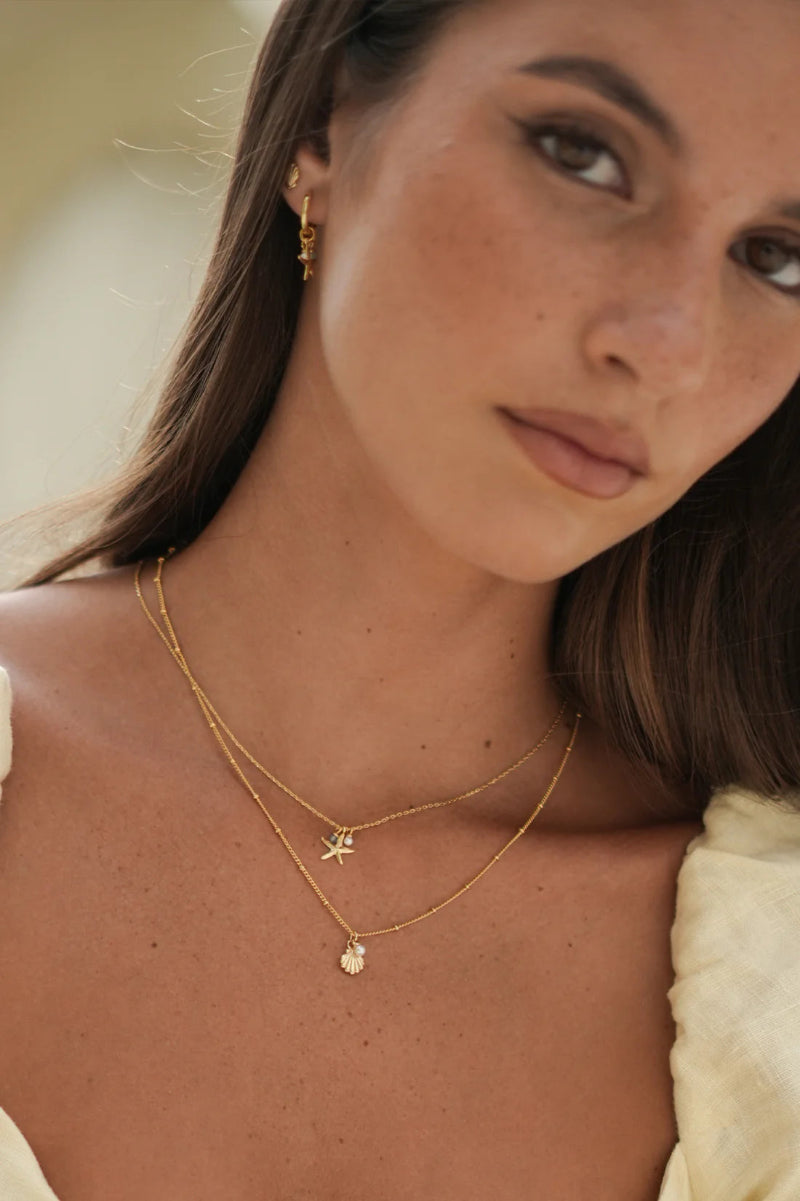 Close-up of a woman wearing gold necklaces with starfish pendants.