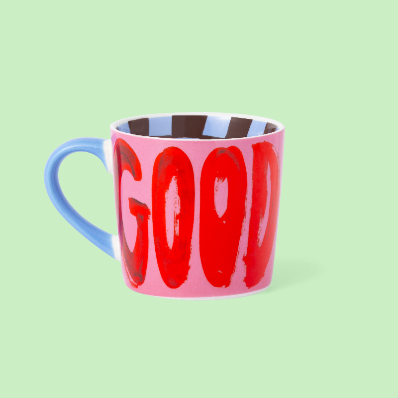 Pink mug with blue handle and red text on a light green background