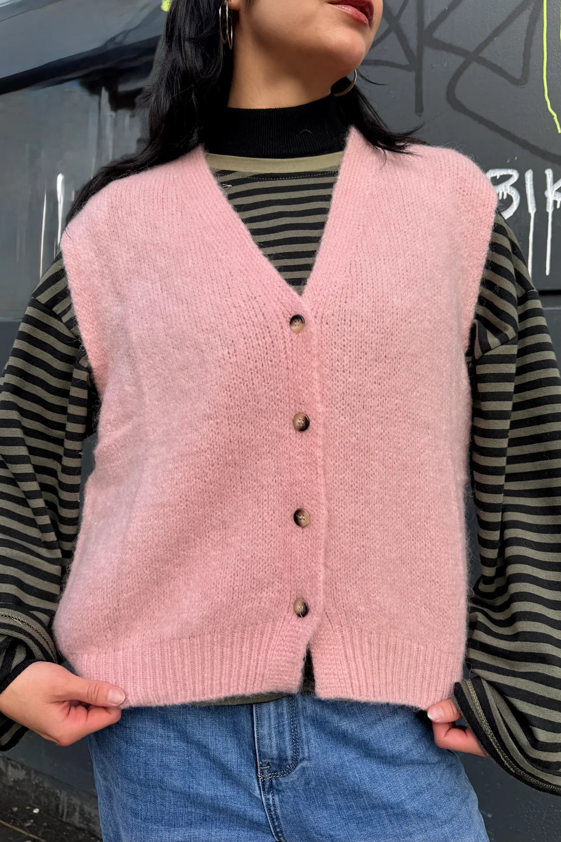 Person wearing a pink knitted vest over a striped shirt with a blurred background