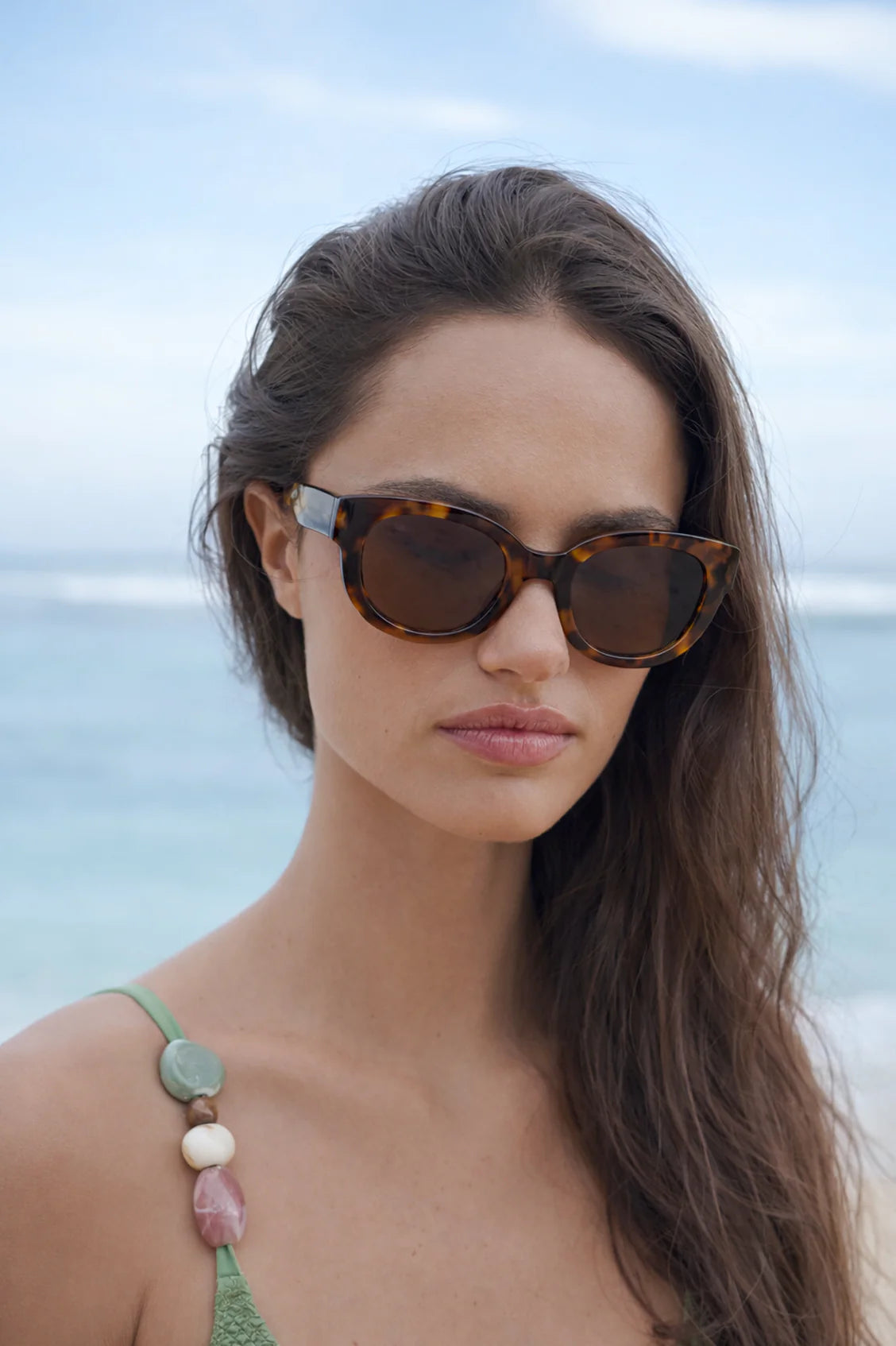 Woman wearing Estella Bartlett Seoul Sunglasses Demi Brown with a beach in the background