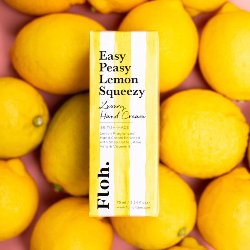 Hand cream box labeled 'Easy Peasy Lemon Squeezy' surrounded by lemons on a pink background