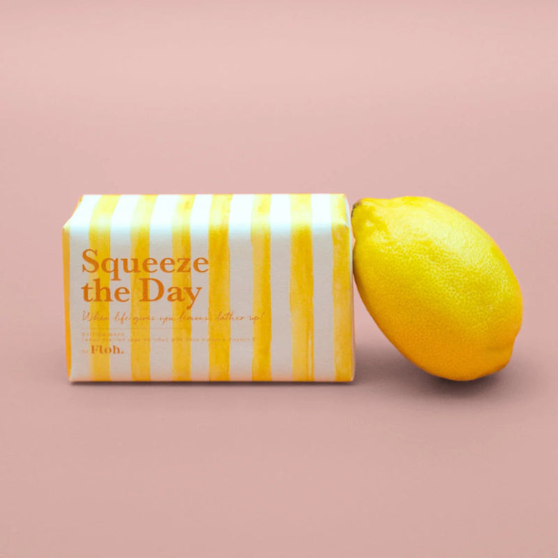 Striped lemon-shaped container with 'Squeeze the Day' text next to a real lemon on a pink background