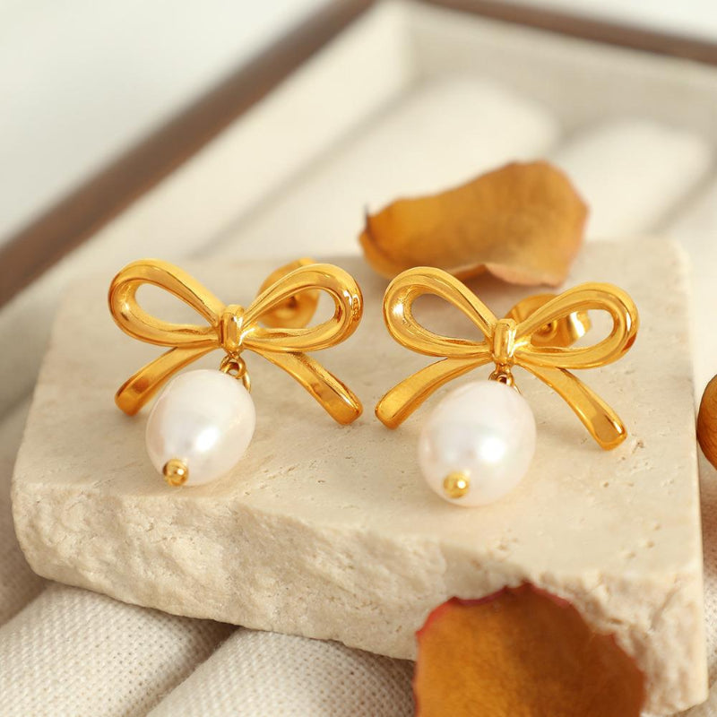 Gold bow-shaped earrings with pearl centers on a stone surface.