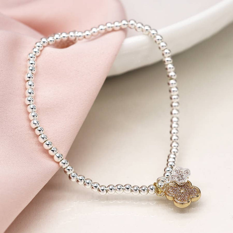Silver beaded bracelet with a gold flower charm held by a hand on a light background