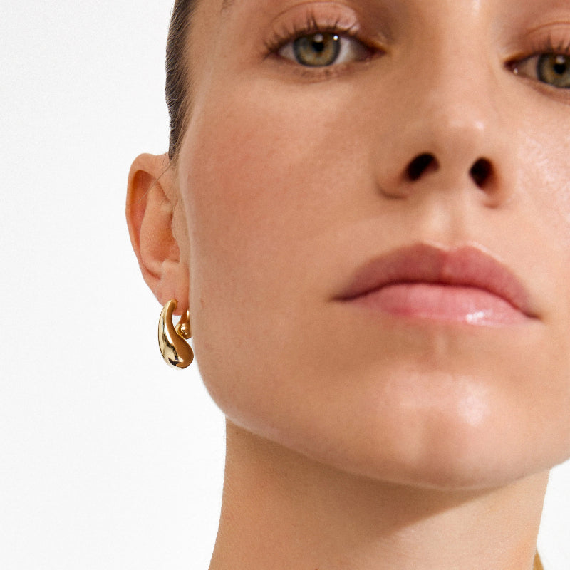 Close-up of a woman wearing gold hoop earrings with a plain background