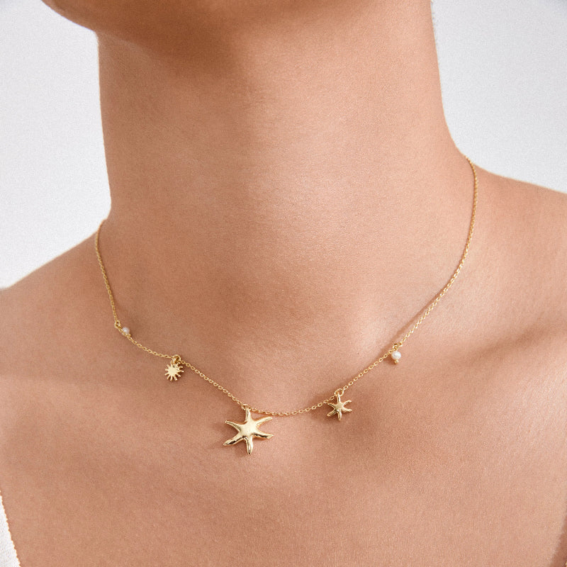 Gold necklace with star-shaped pendants on a person against a white background