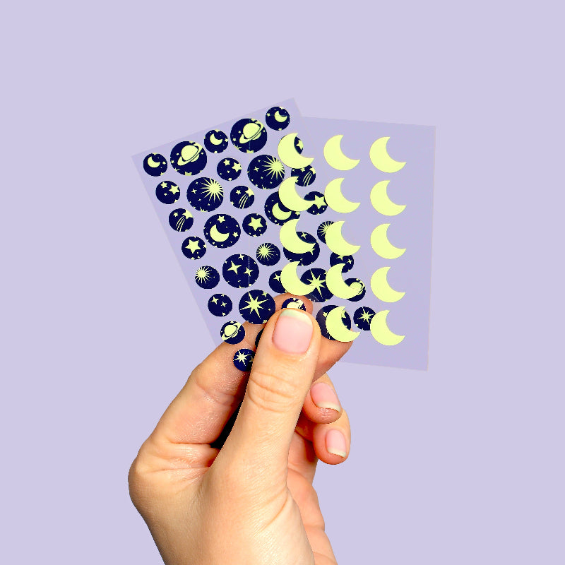 Hand holding a sheet of celestial-themed stickers against a light purple background
