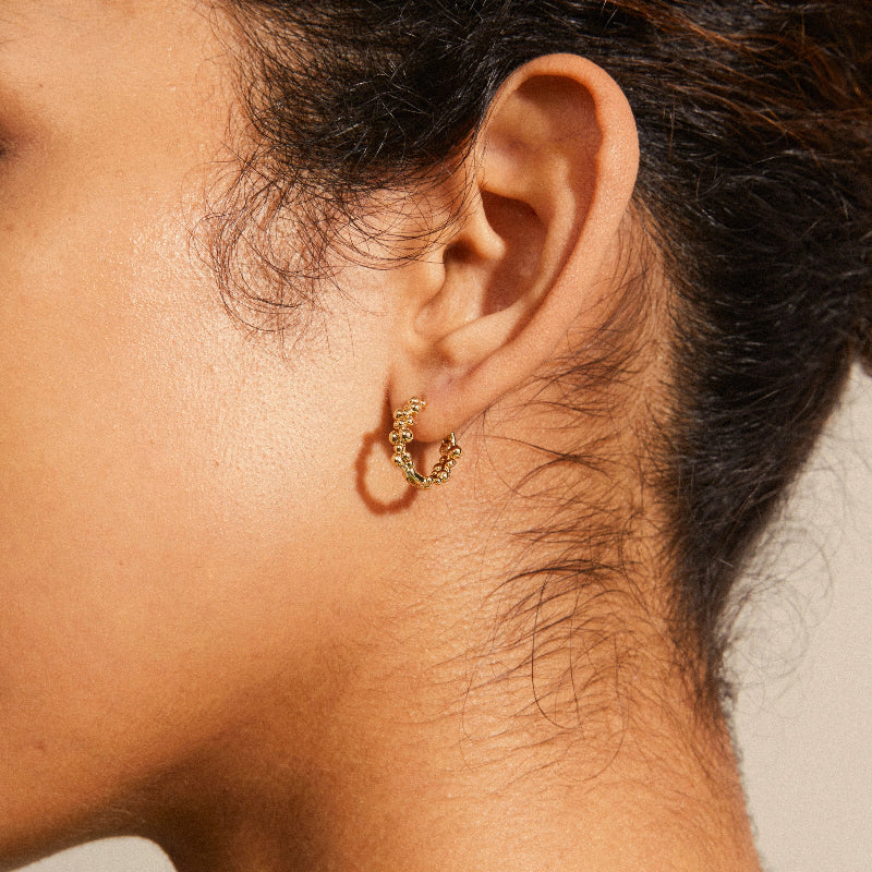 Close-up of an ear wearing a gold hoop earring with a neutral background