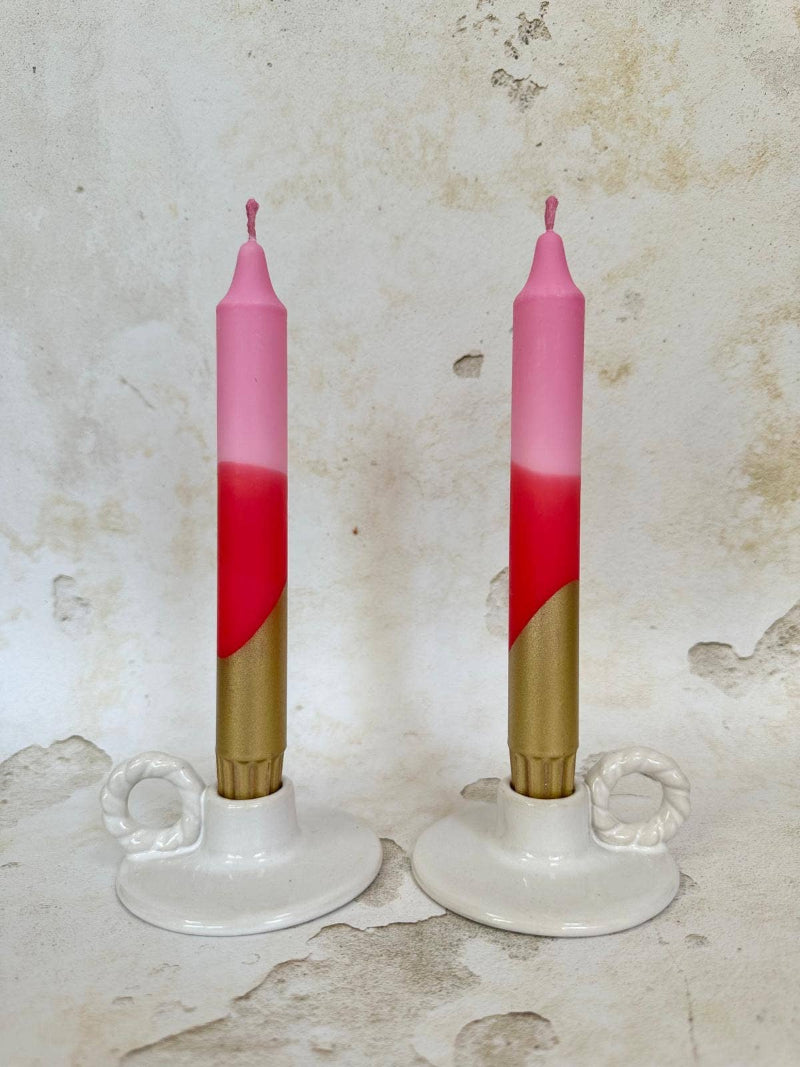 Two pink and gold candles on white candle holders against a textured beige background